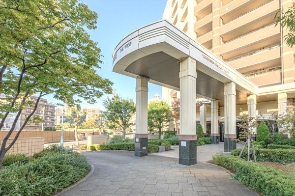 緑の植栽が映えるベージュのタイルに包まれたマンションエントランス