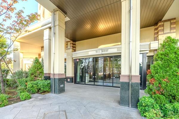 緑の植栽が映えるベージュのタイルに包まれたマンションエントランス